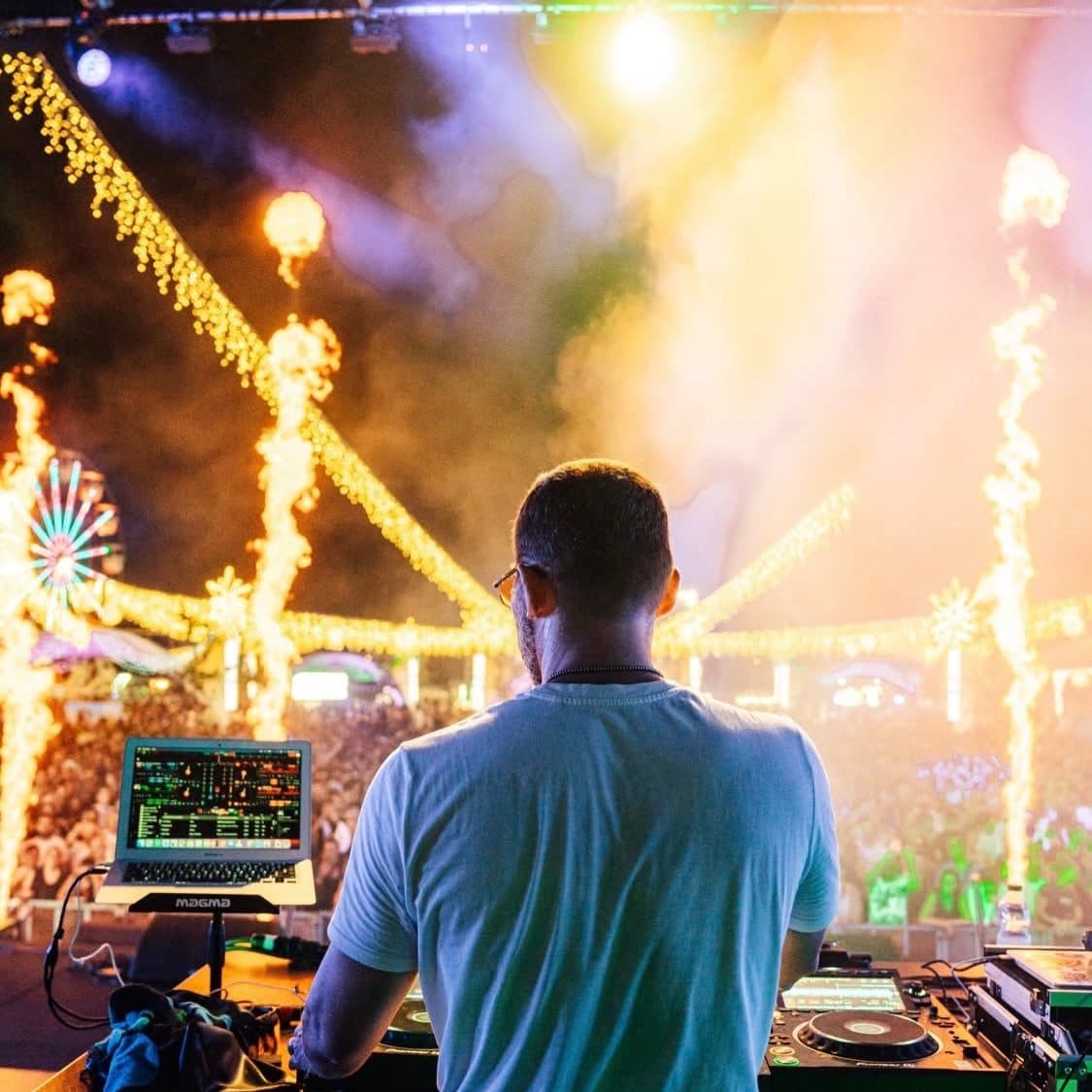 A DJ seen from behind at the desk during a village festival