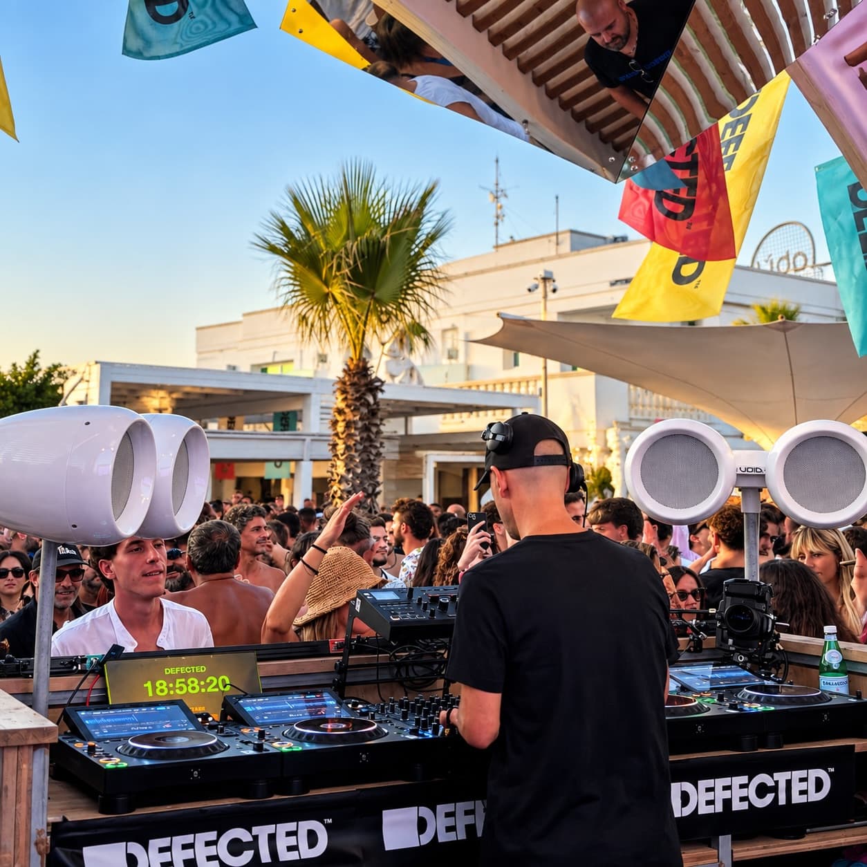 A DJ booth with speakers and flags above the floor, in the afternoon